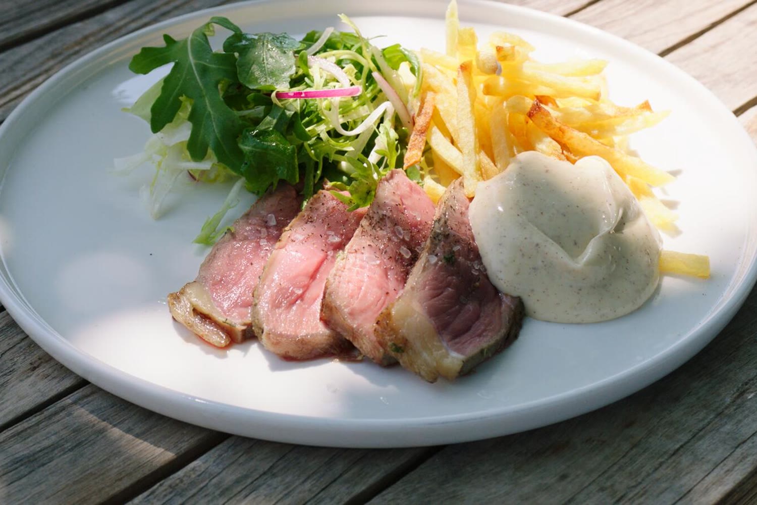 Steak-friet met salade en romige saus op een houten terrastafel
