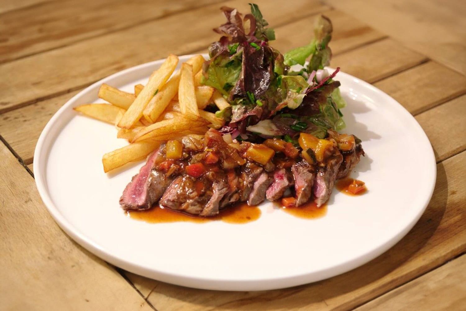 Gesneden steak met warme groenten, friet en salade op een wit bord