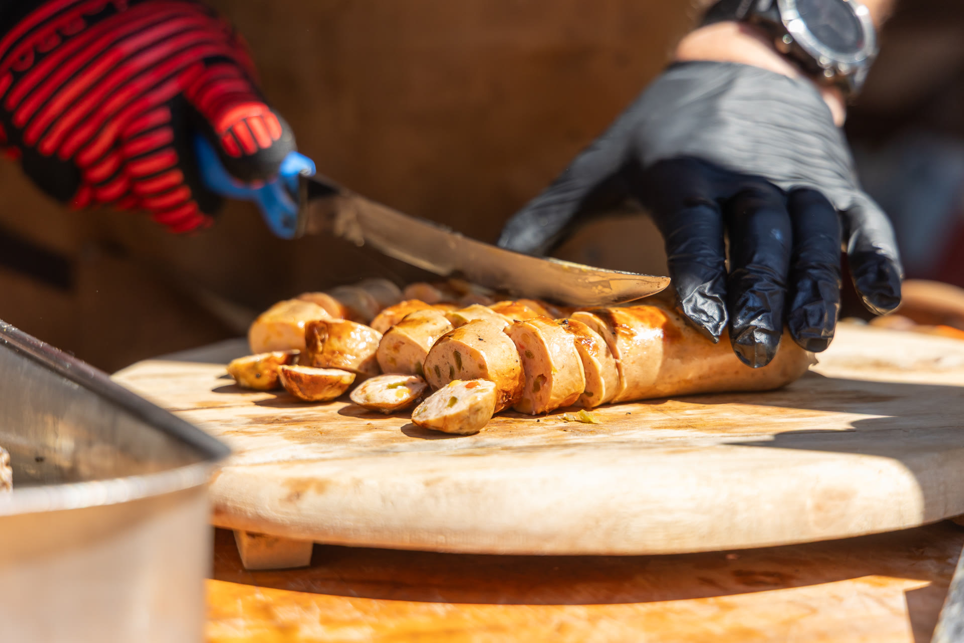 Gegrilde worsten worden met handschoenen aangesneden op een houten plank