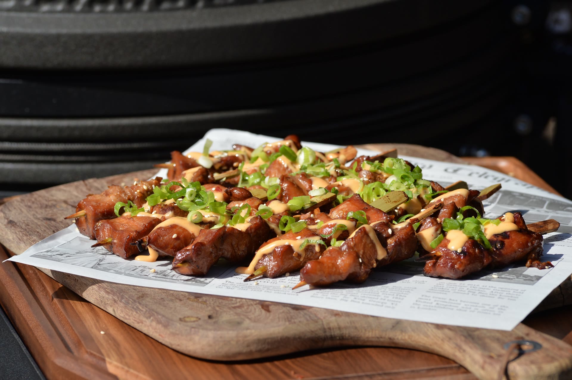 Gegrilde vleesspiesjes met saus en lente-ui liggen op een houten plank