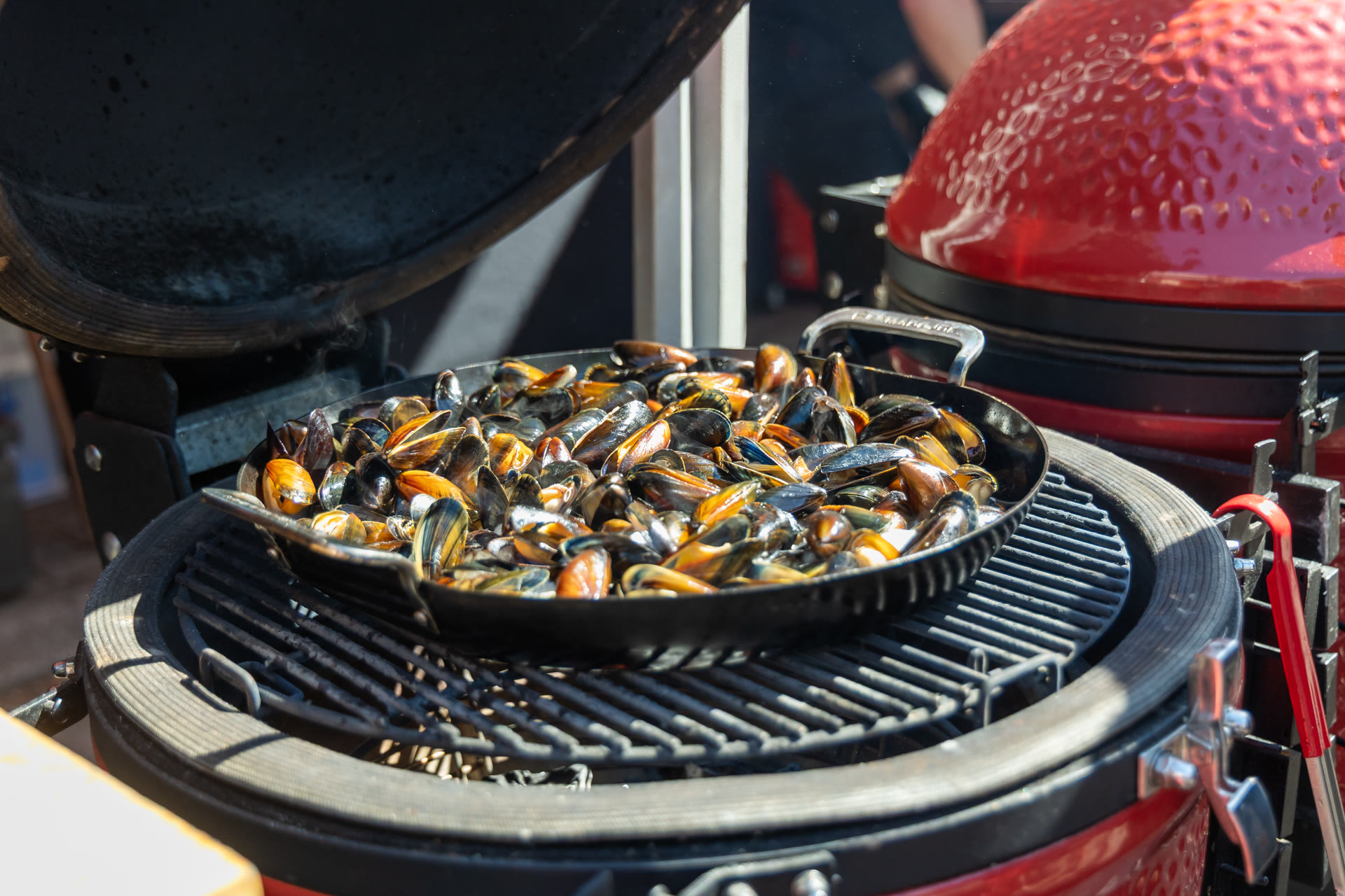 Een pan mosselen gaart op een open kamado in zomers daglicht