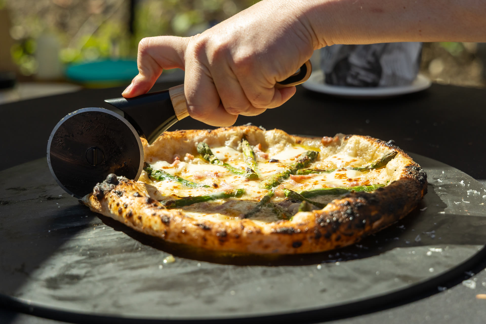 Een pizza met asperges wordt in de buitenkeuken aangesneden
