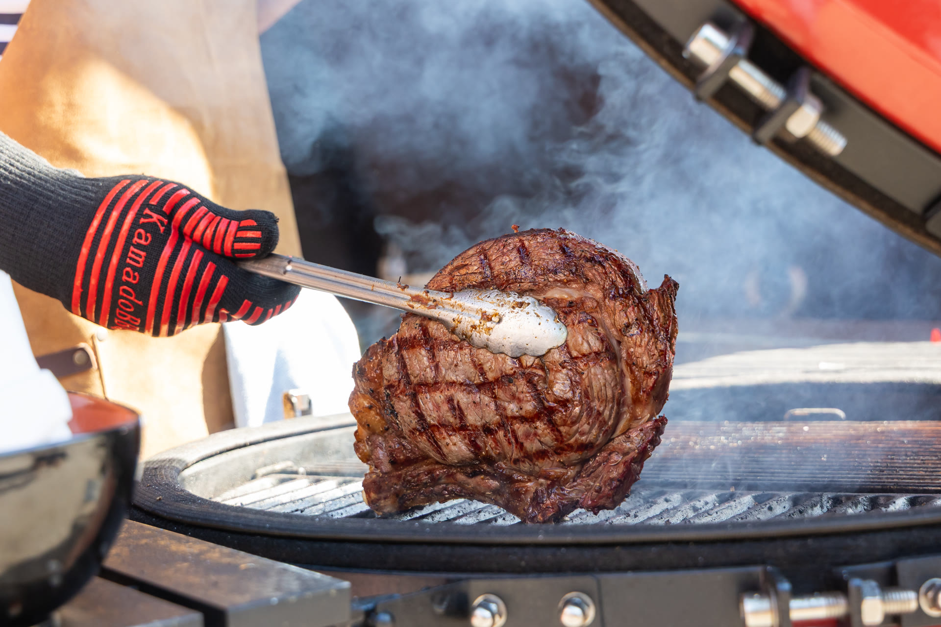 Een groot stuk rundvlees wordt boven een rokende kamado gehouden